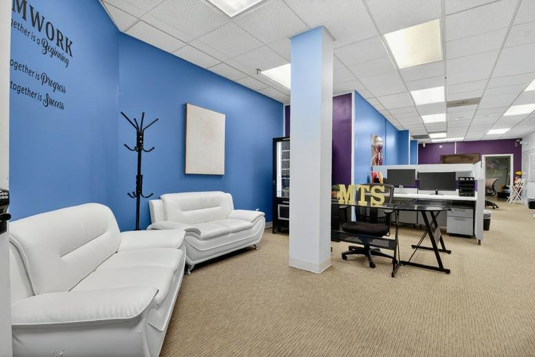 Lounge area at 8101 Sandy Spring Road, Suite 280 with white sofas and teamwork wall decal.