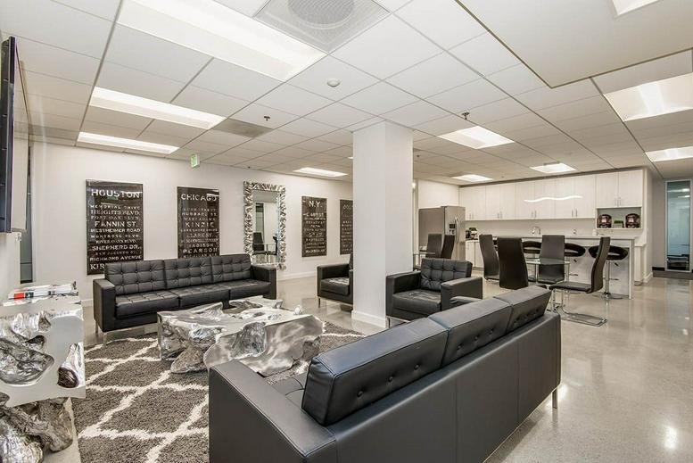 Contemporary lounge with black leather sofas, a textured rug, and a white kitchen in the background.