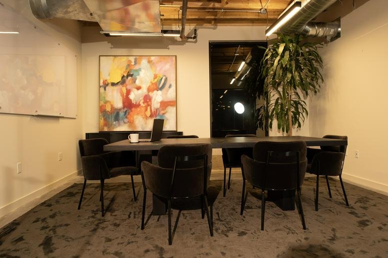 Small meeting room with a dark table, plush black chairs, and a colourful abstract painting.