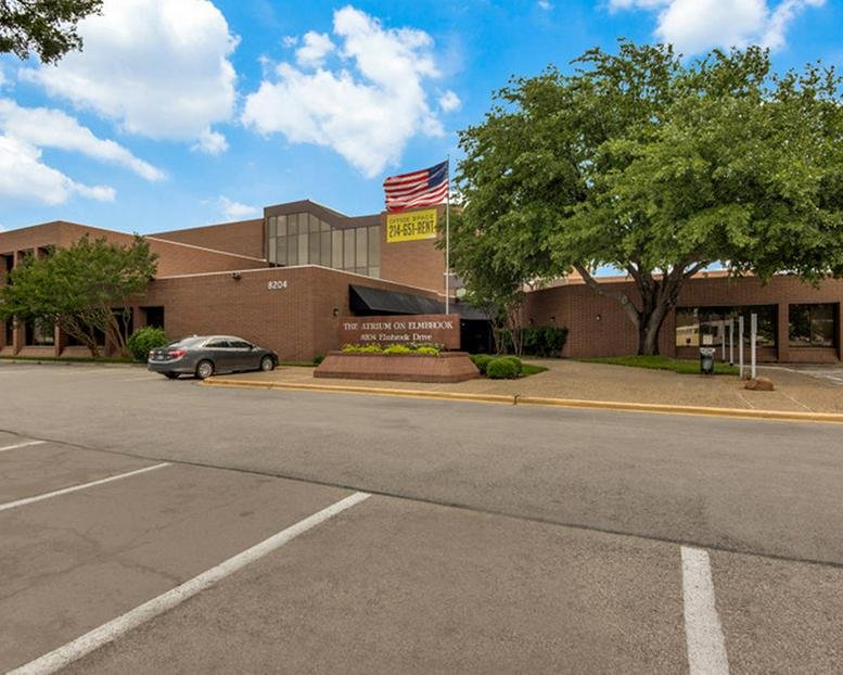 Wide street-level view of the brick office building with manicured landscaping and a flagpole.