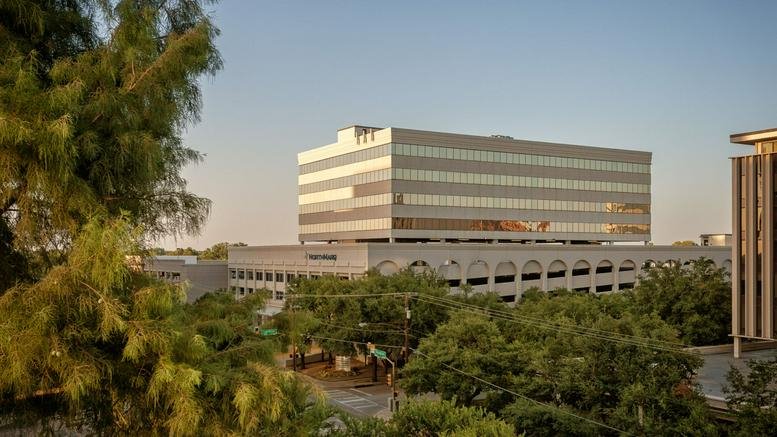 Distant view of the glass and stone office building nestled behind lush green trees.