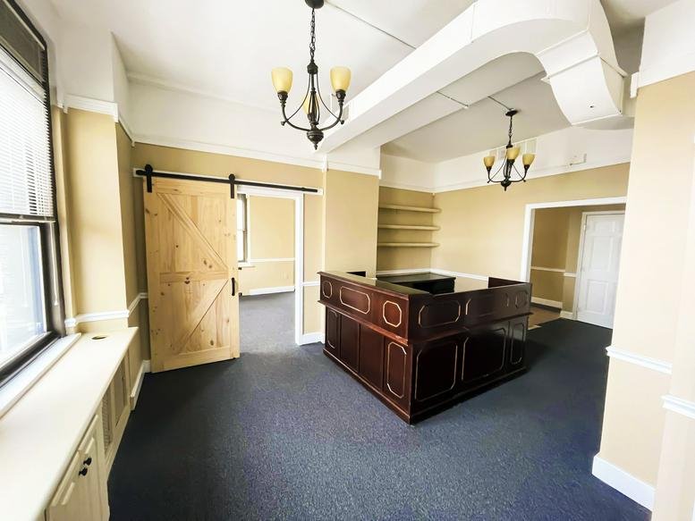 Reception area with a dark wood front desk, warm beige walls, and a light wood barn door.