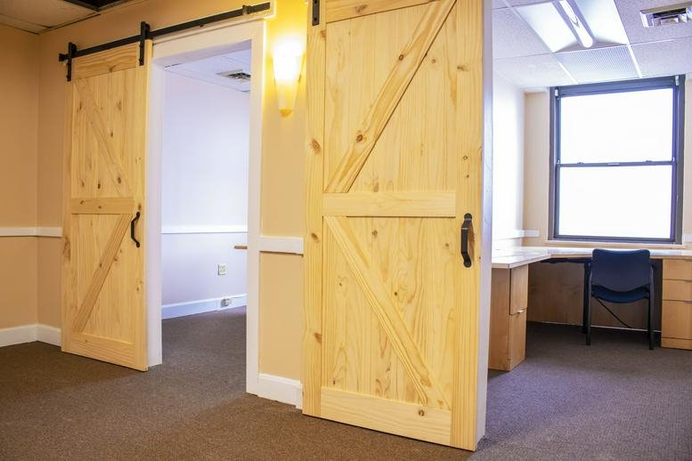 L-shaped wooden desk in an office with light-toned sliding barn doors.
