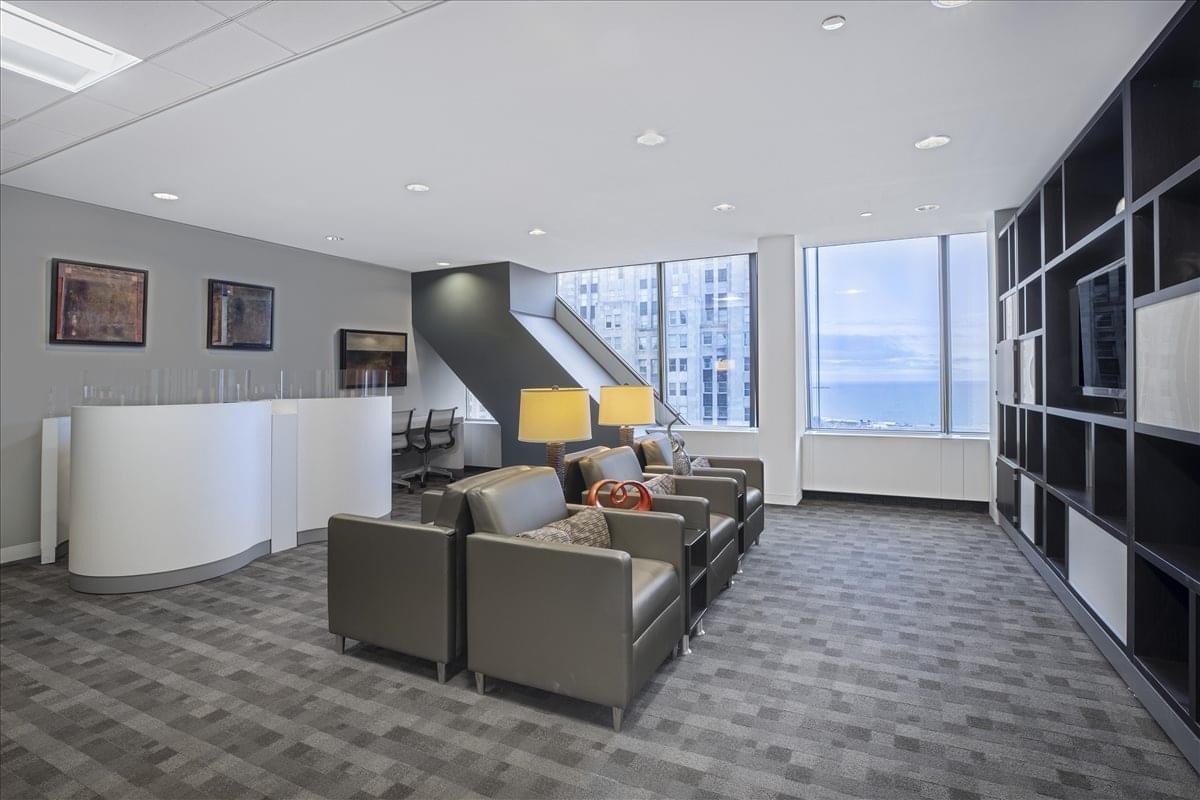 Modern lounge area with grey armchairs, bookshelves, and views from the John Hancock Center.