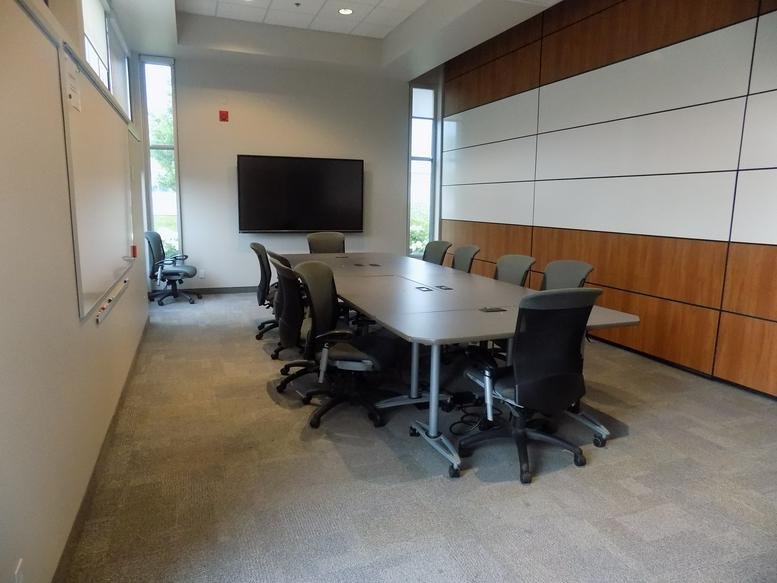 Meeting room at 92 Caplan Avenue, Suite 309, featuring a long table, wall-mounted screen, and wooden paneling.