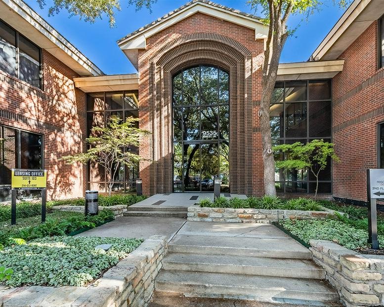 Exterior entrance of the brick building at 9535 Forest Ln featuring a large arched glass facade.