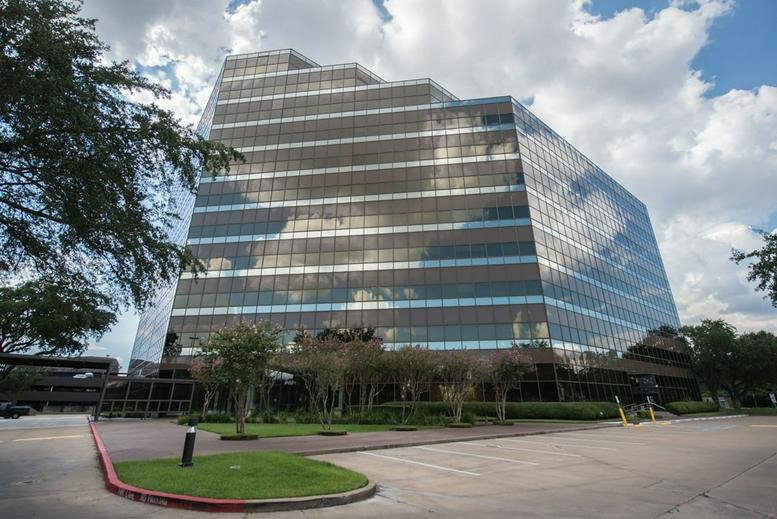 The mirrored glass exterior of the multi-story 9801 Westheimer building under a cloudy sky.