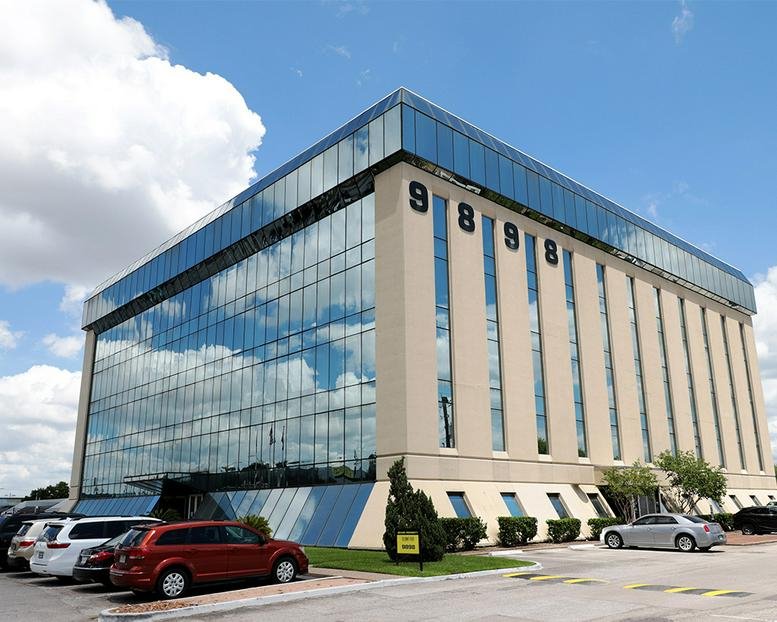 Wide exterior shot of the commercial building and parking lot under a blue sky.