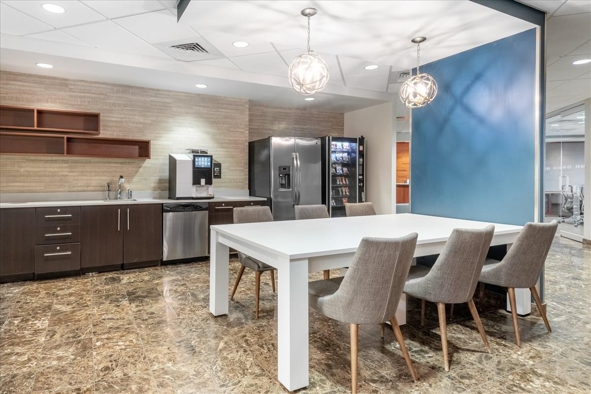 Modern breakroom featuring a white dining table, grey upholstered chairs, and a blue feature wall.