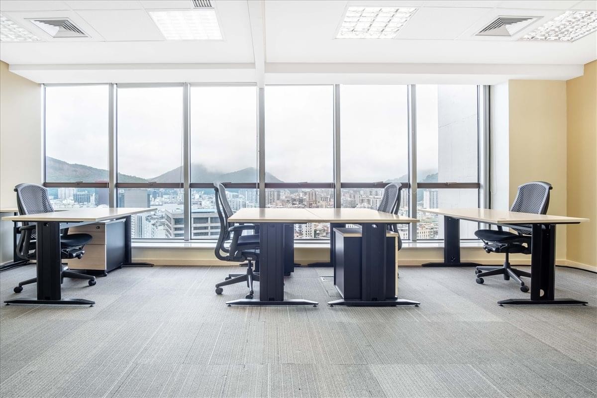 Open-plan office with multiple desks and floor-to-ceiling windows showing city views.