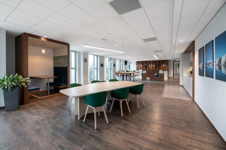 Spacious communal lounge at Ed Alpha Business featuring a long wooden table, green chairs, and a cozy seating booth.
