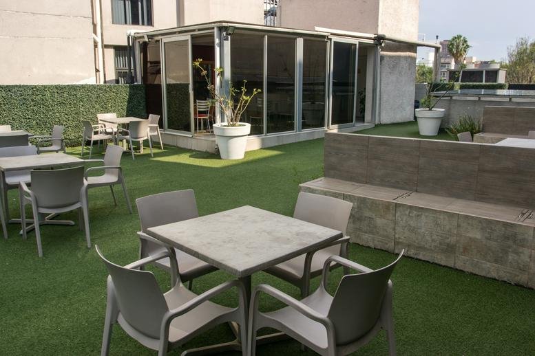 Outdoor rooftop terrace at Av. Baja California No. 274 with artificial grass, dining tables, and a glass-walled lounge.