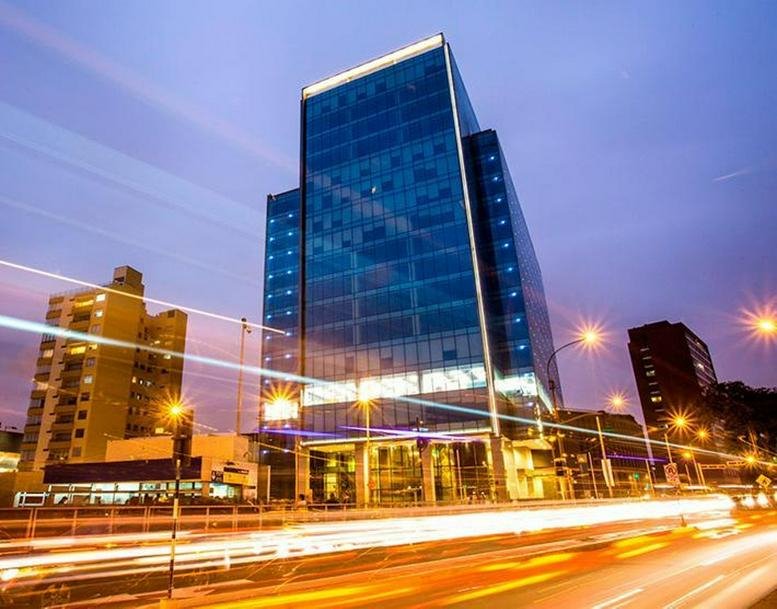 Exterior view of the glass-facade Av. Benavides 1180, Piso 6 building at dusk with light trails.