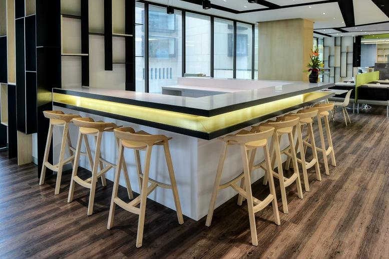 Modern communal cafe area featuring a white wrap-around bar with wooden stools and warm lighting.