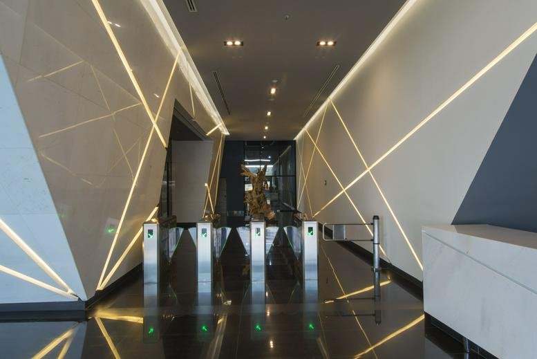 Sleek entrance hallway with geometric light strips on the walls and security turnstiles.