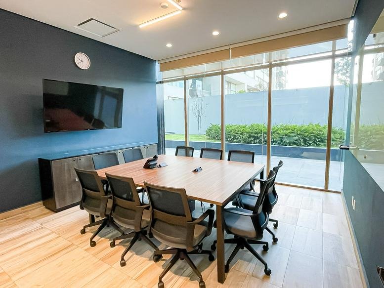 Professional conference room featuring a large square table and a wall-mounted screen.