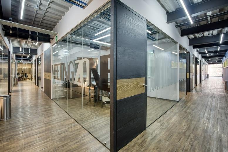 Wide glass-walled office corridor with wooden floors and meeting rooms at Av. Jinetes No. 7, piso 2.
