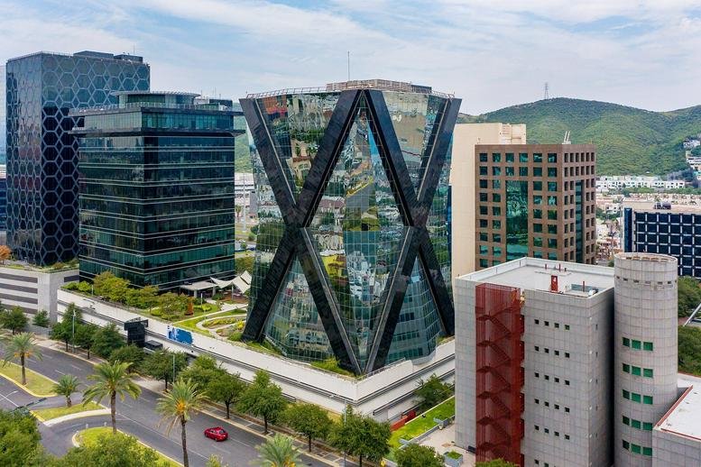 Exterior view of the glass-facade Av. Pedro Ramírez Vázquez 200-1 building with mountain backdrop.