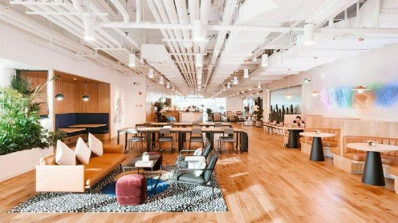 Spacious reception and lobby area with exposed ceiling pipes, plush leather sofas, and colorful wall art.