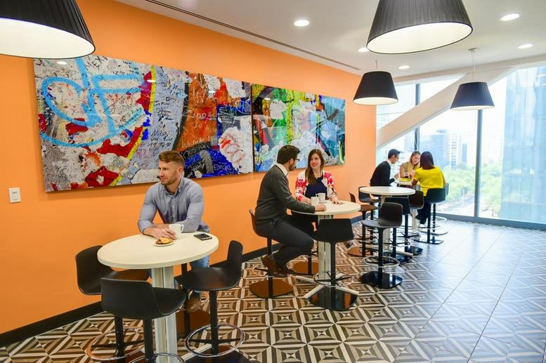 Vibrant breakout area featuring a large colorful abstract mural, orange walls, and people at bistro tables.