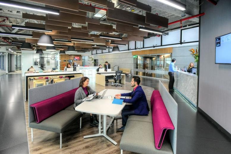 Bright reception area with a marble desk, vibrant pink seating, and wood-slatted ceiling panels.