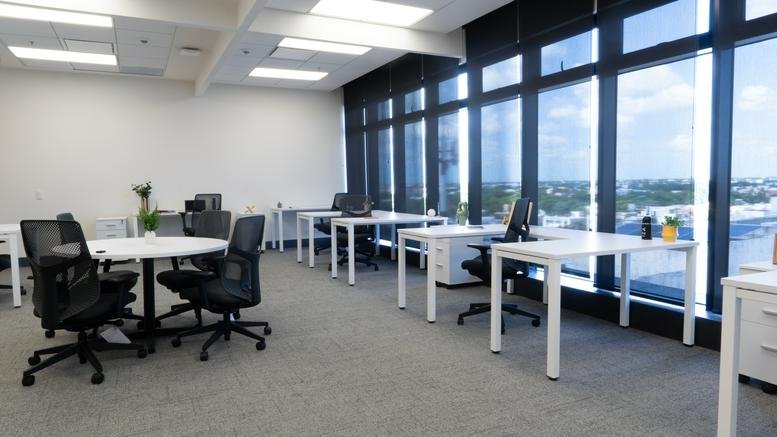 Spacious open-plan office with white desks, ergonomic chairs, and large windows.