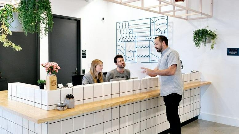 Reception desk at Aventine, 8910 University Center Lane with white tiling, wood accents and hanging plants.