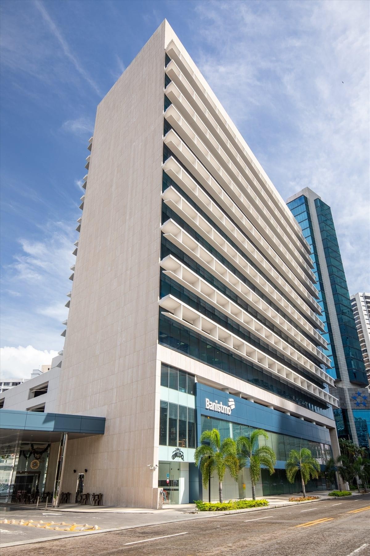 Exterior view of the light-toned Banistmo Tower with tiered balconies and street-level palms.