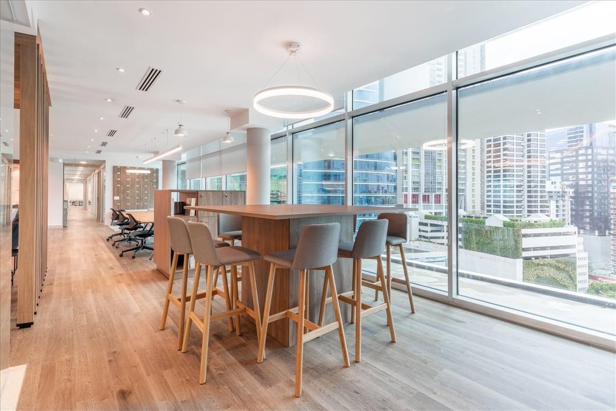 High-top coworking table with grey stools next to large windows with city views.