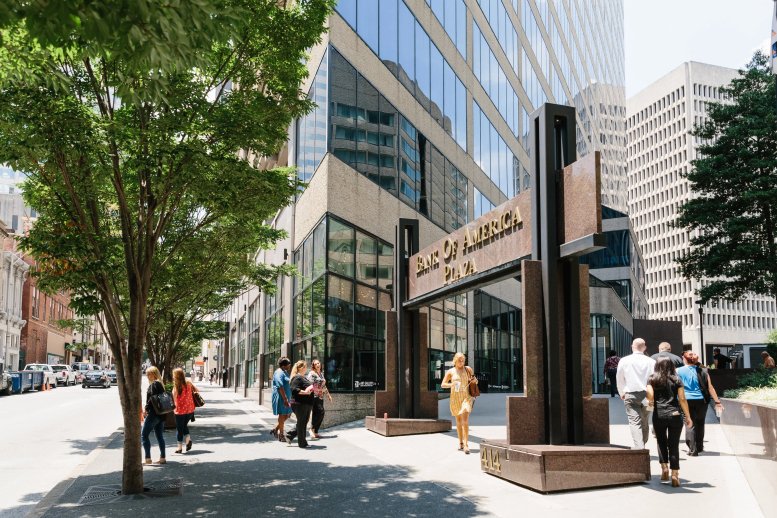 Street-level exterior view of the Bank of America Plaza entrance with pedestrians and lush trees.