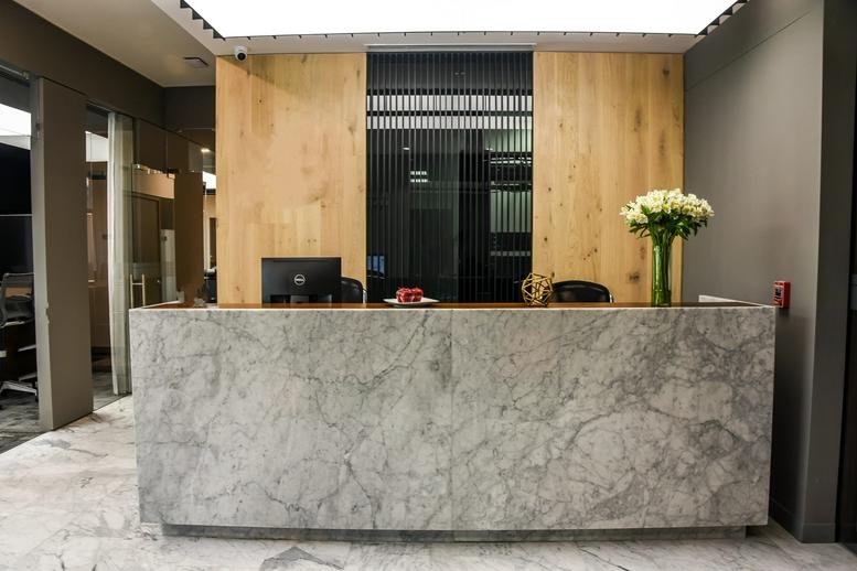 Modern reception desk with a grey marble-patterned facade and wooden wall panels.