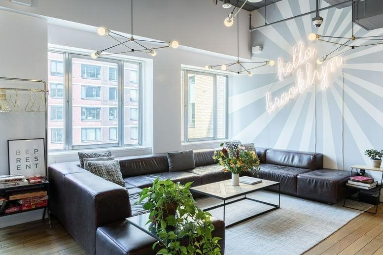 Bright lounge area with leather seating, potted plants, and a Hello Brooklyn neon sign.