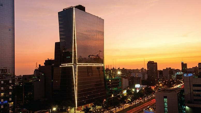 Exterior view of the illuminated glass facade at Ca. Las Orquídeas 444 during a sunset city skyline.