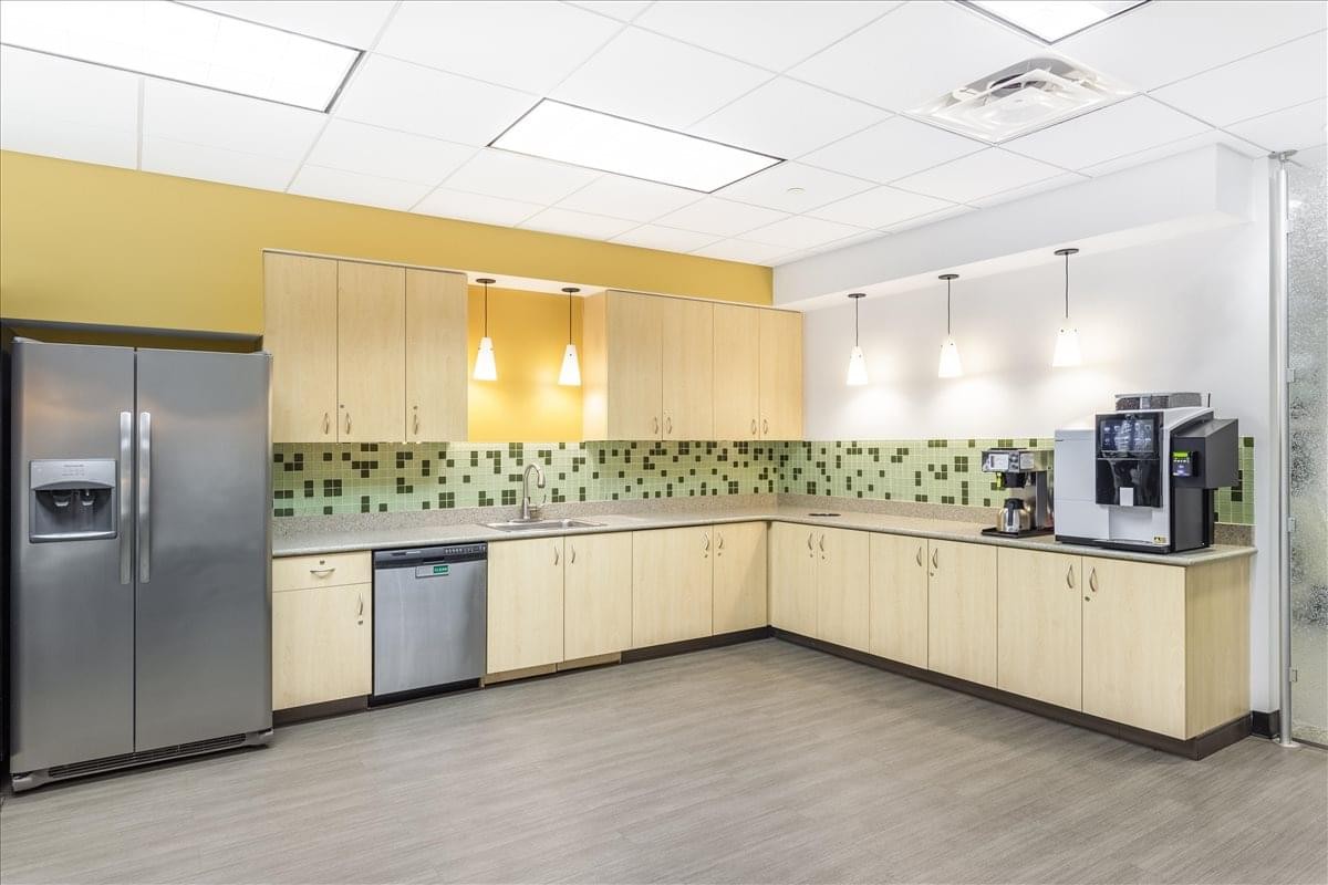 Modern communal kitchen at Calder Plaza with light wood cabinetry, stainless steel appliances, and a coffee machine.