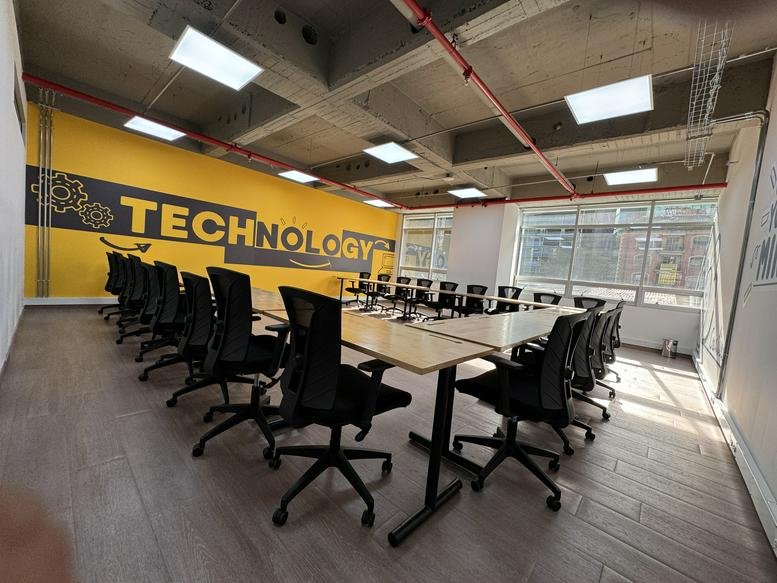 Conference room with a U-shaped table arrangement and a yellow accent wall with technology graphics.