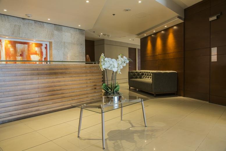 Modern building reception with a wood-slat desk, grey sofa, and white orchid centerpiece.