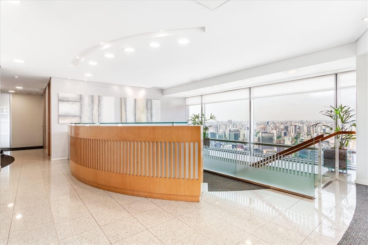 Bright reception area with a curved wooden desk and floor-to-ceiling windows overlooking Sao Paulo.