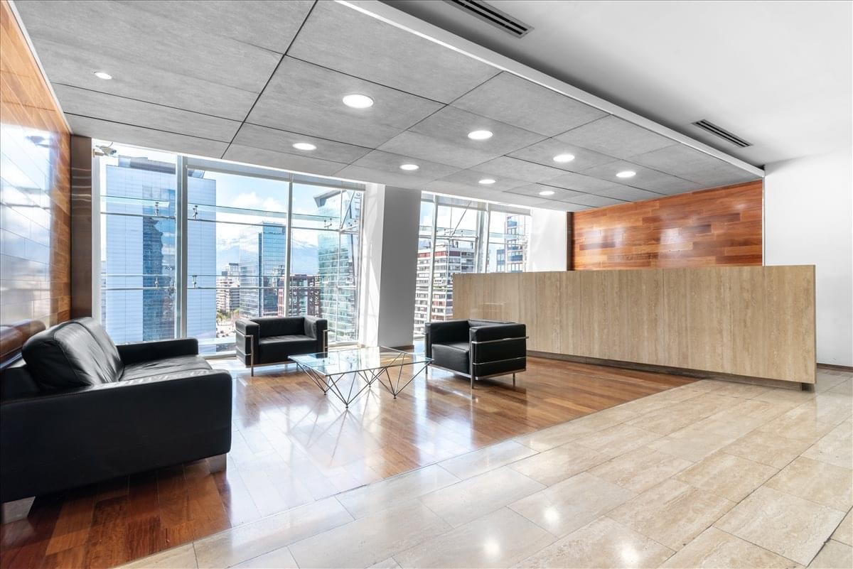 Reception area featuring a large wooden desk, black leather sofas, and city views.