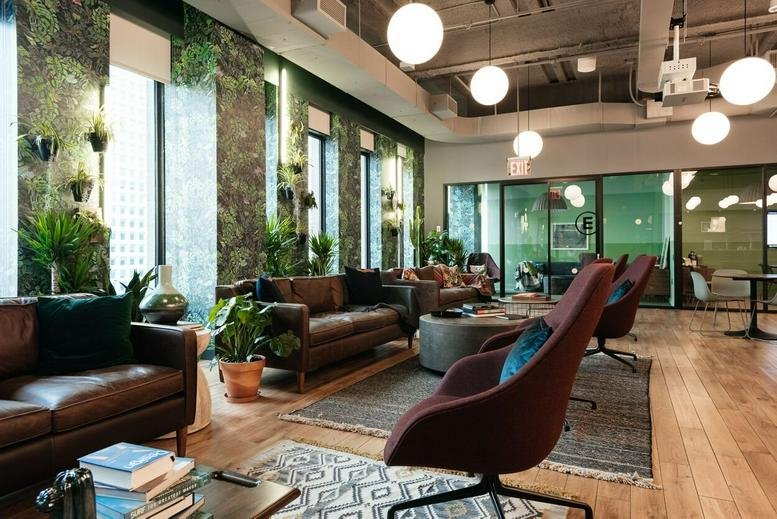 Spacious communal lounge at 85 Broad Street with leather sofas, hanging globe lights, and lush plant walls.