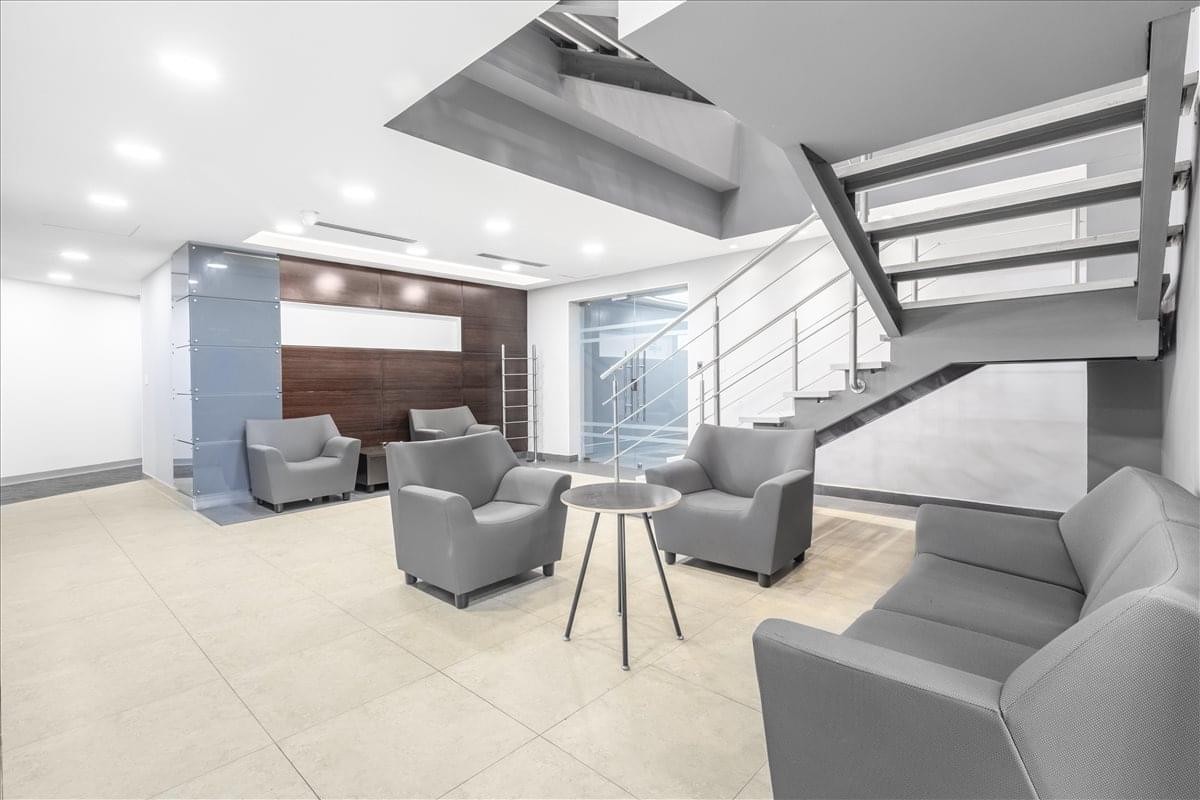 Modern lobby area of Financial Park Tower with grey armchairs, a central table, and an open staircase.