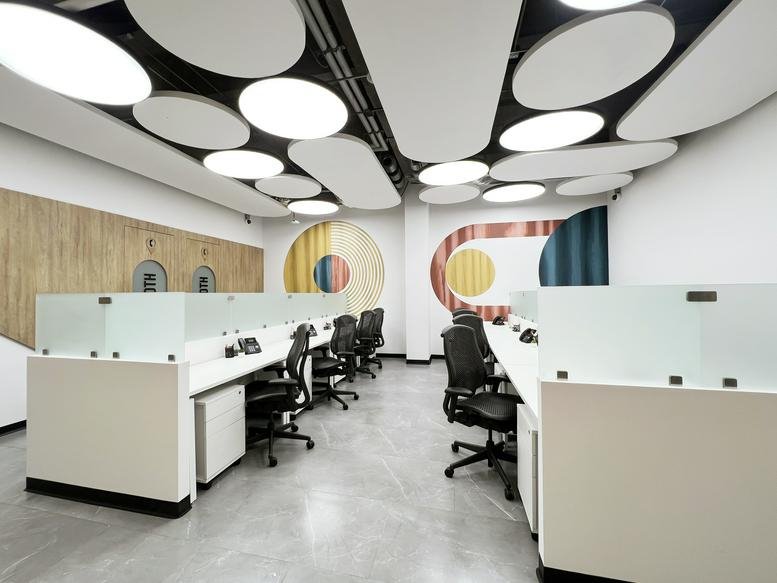 Open-plan office area with rows of white desks and distinctive circular white acoustic ceiling clouds.