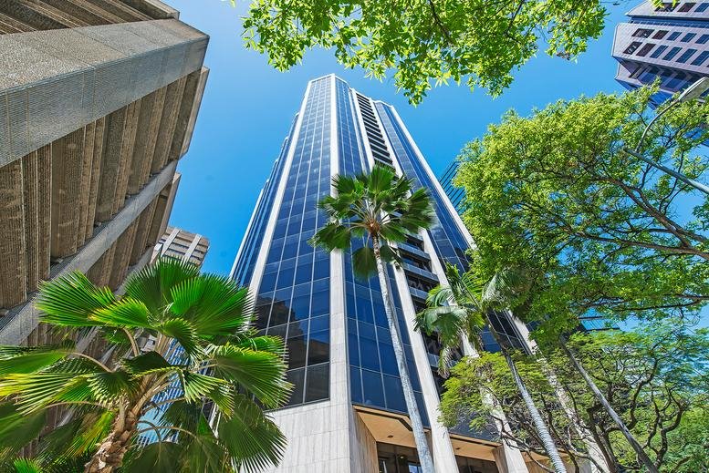 Exterior view of the skyscraper at 1003 Bishop Street, Suite 2700, framed by lush tropical trees.