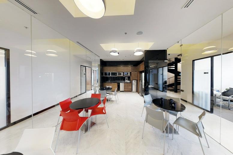 Vibrant communal breakout area with red chairs, white floors, and a kitchen in the background.