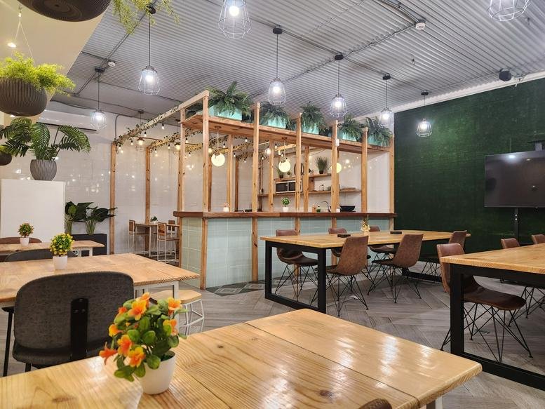 Spacious coworking lounge with a mix of shared tables, green walls, and hanging pendant lights.