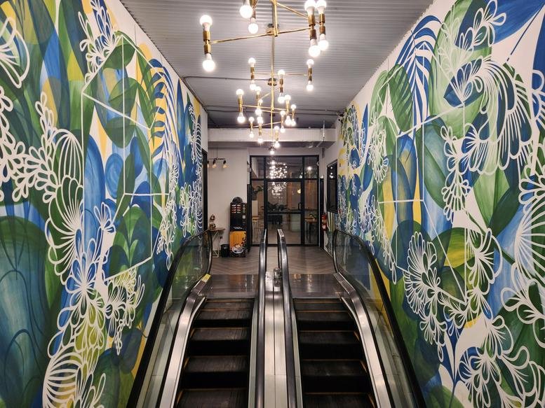 Entrance to Metro Hub Cowork featuring colorful tropical mural walls and an escalator.