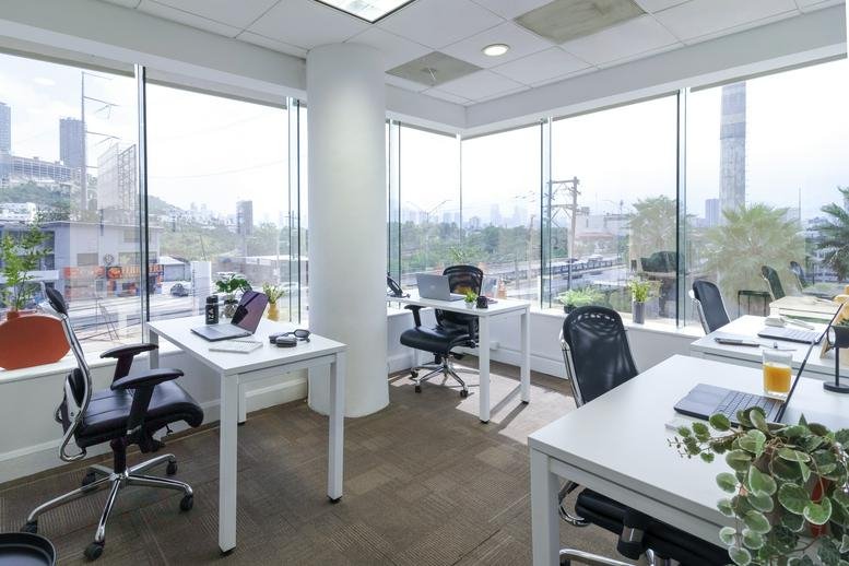 Bright shared office space with white desks and floor-to-ceiling windows overlooking the city.