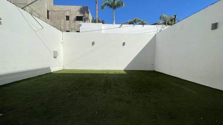 Outdoor courtyard at En Octava Workspaces featuring a large green turf area and white walls.