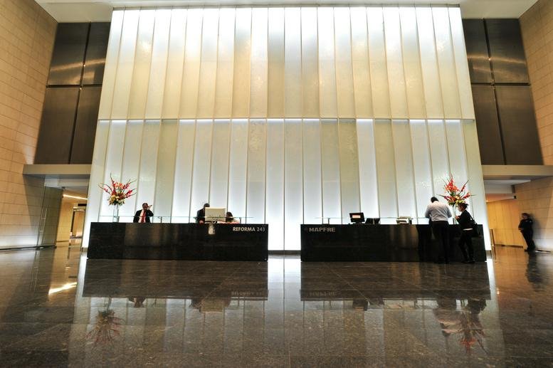 Modern building reception area with a large glowing back-lit wall and dark stone floors.