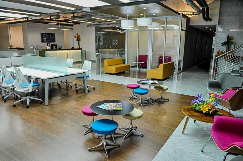 Spacious coworking lounge with colorful seating, wooden floors, and a reception desk in the background.