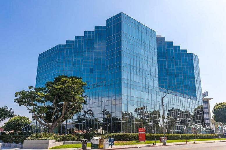 The glass-facade exterior of (PCH) 5150 E. Pacific Coast Hwy under a clear blue sky.